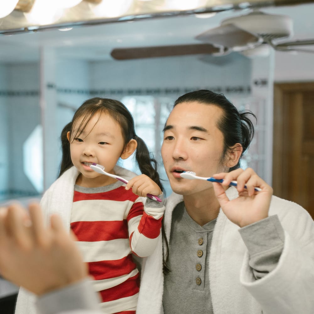 A father and his young daughter brushing their teeth side by side